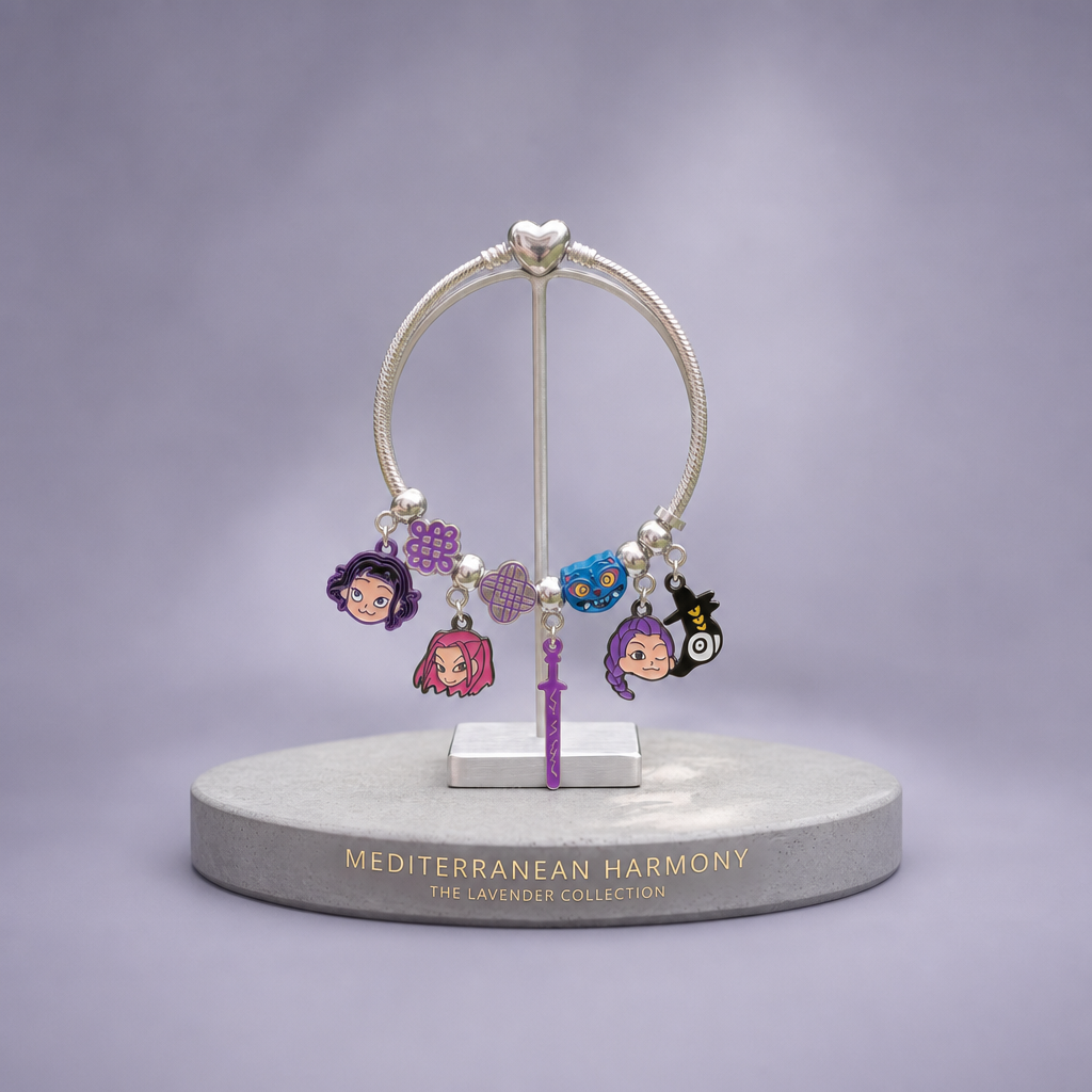 A silver charm bracelet displayed on a stand, featuring multiple colorful enamel charms including cartoon-style faces and a purple heart, set against a soft lavender-gray gradient background with a branded display base reading 'MEDITERRANEAN HARMONY THE LAVENDER COLLECTION'.